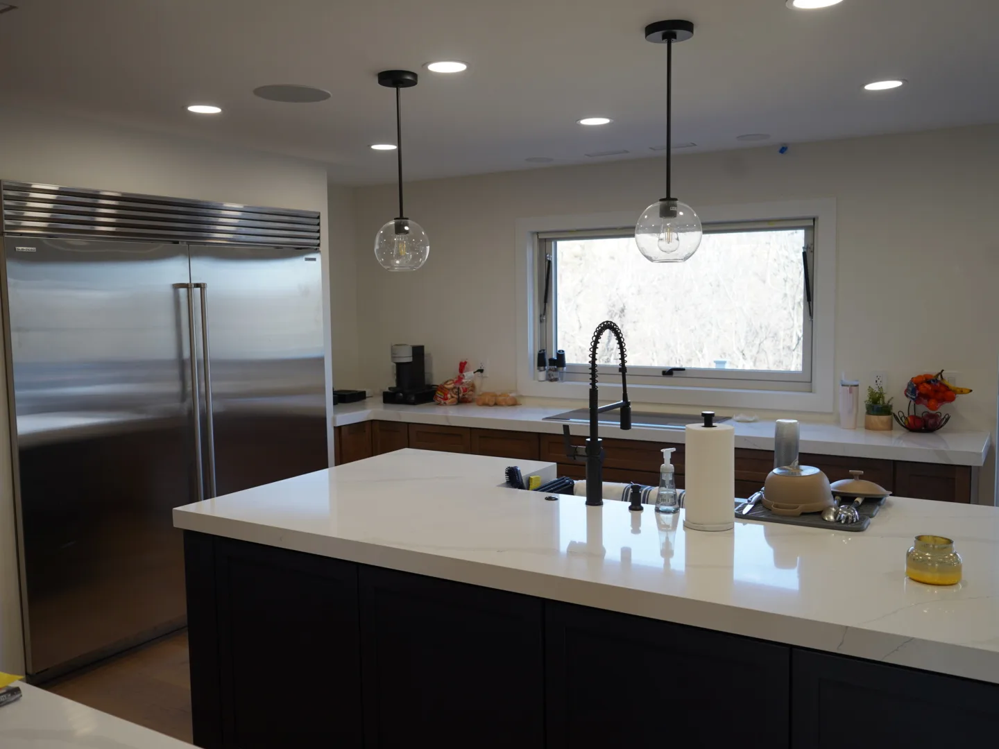 Kitchen island with a white countertop, dark base cabinets, pendant lights, and an appliance wall.