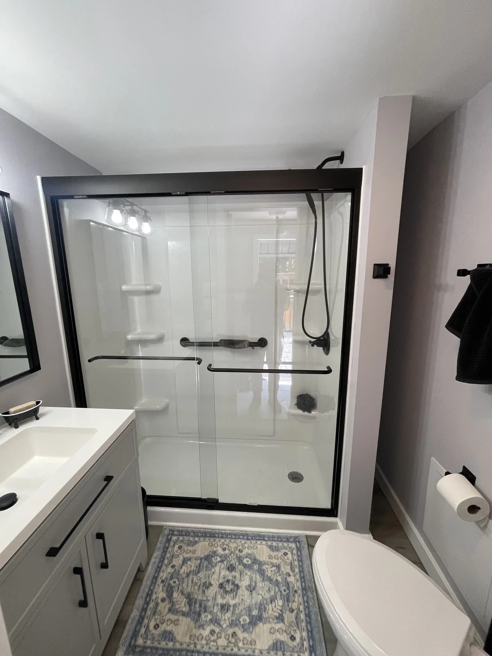 Bathroom with a white shower enclosure, dark frame, and gray vanity.