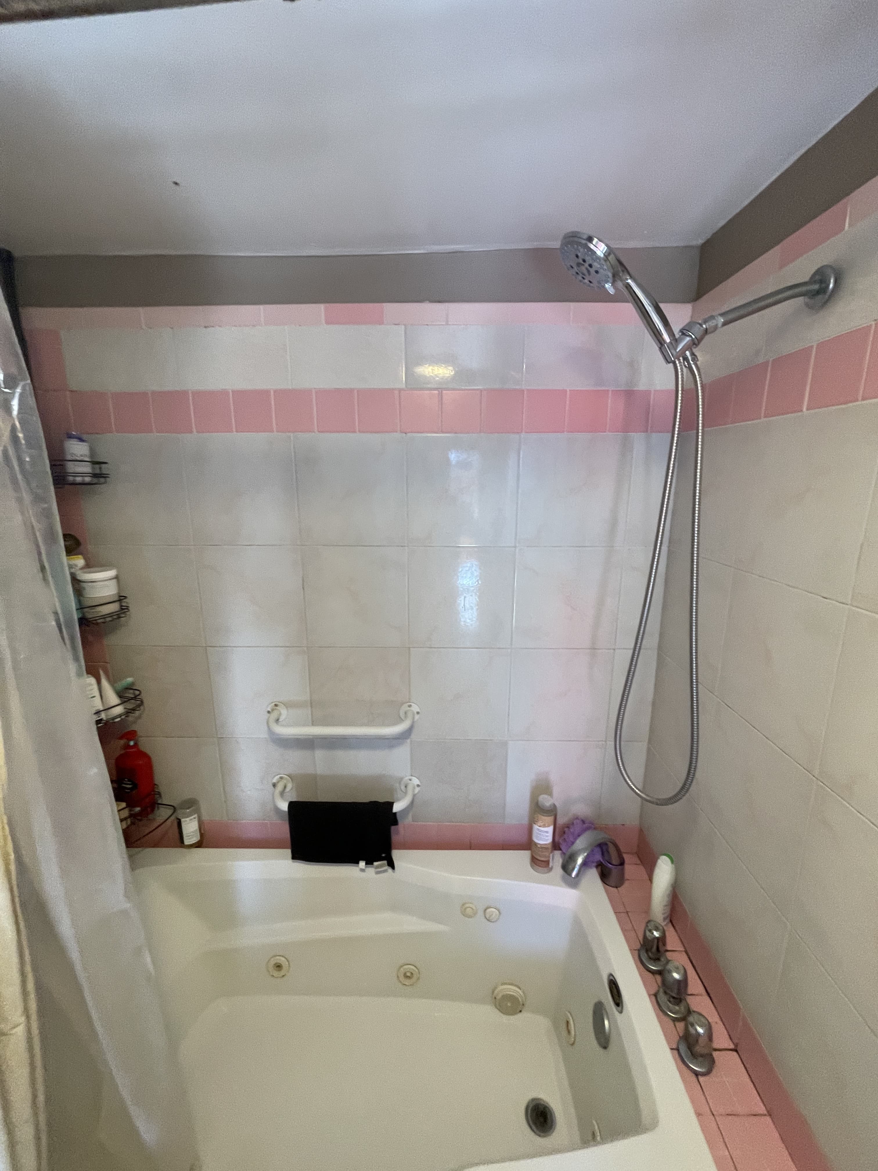 White jetted tub with pink tile bands, grab bars, and a wall-mounted handheld shower.