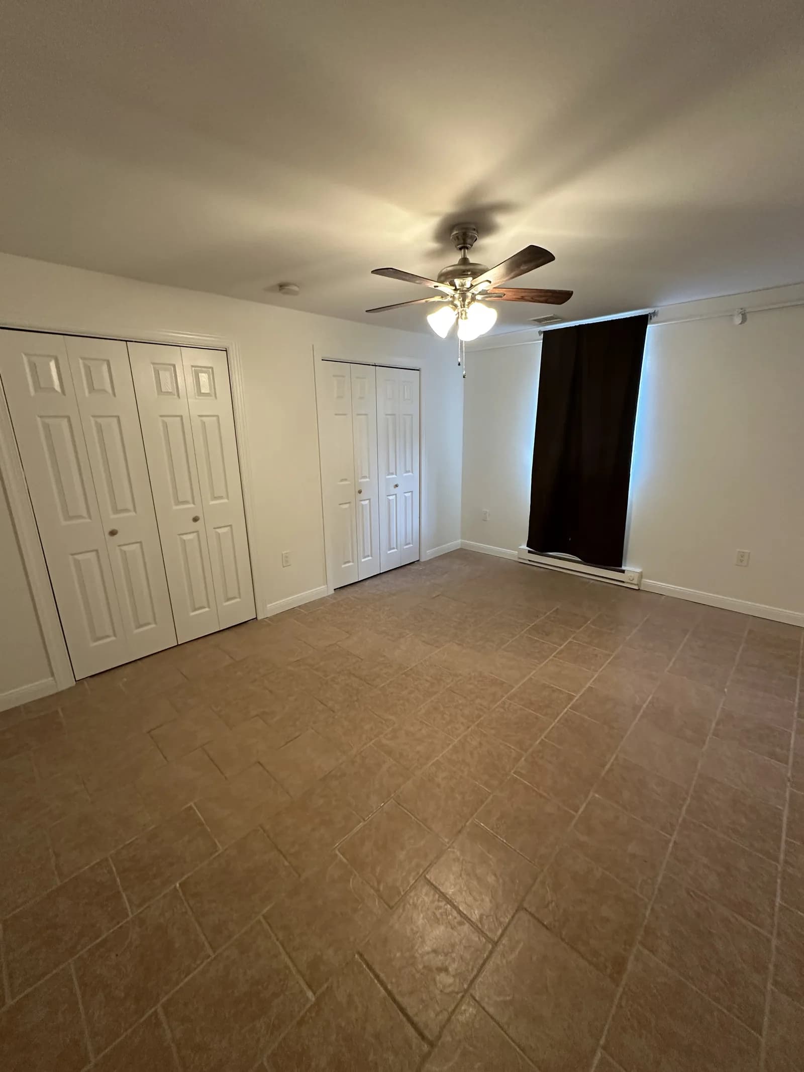Room with smooth white walls, white closet doors, a ceiling fan and a tile floor.