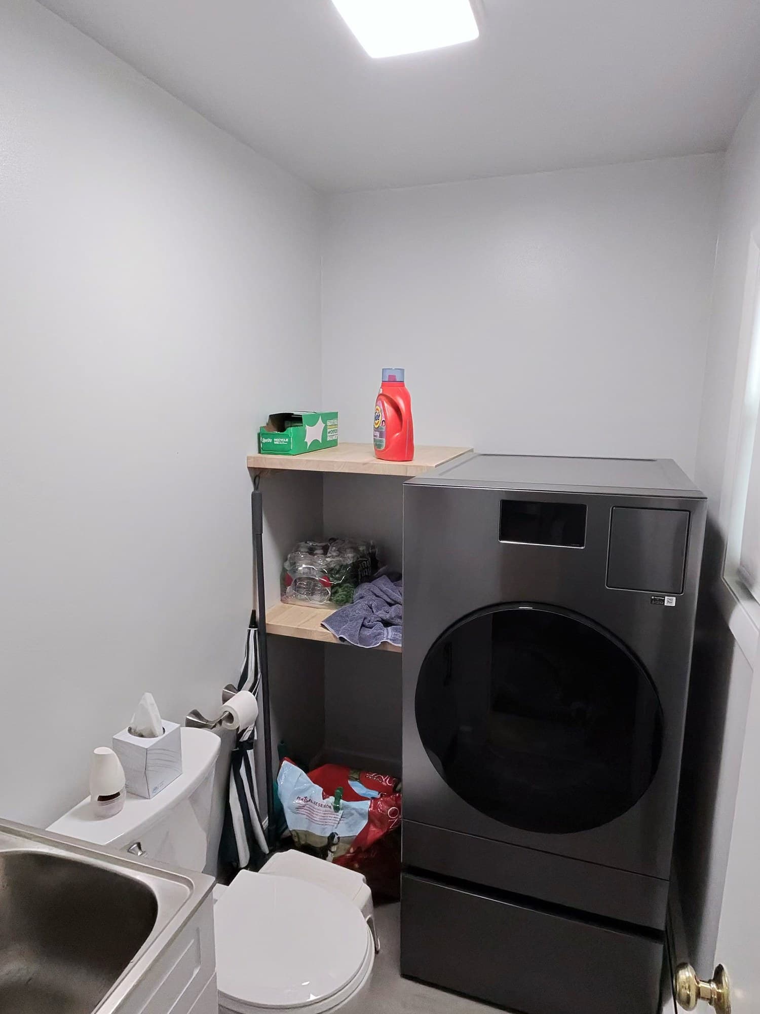 Vanity with stainless utility sink, white toilet, and light wood shelving after remodel.