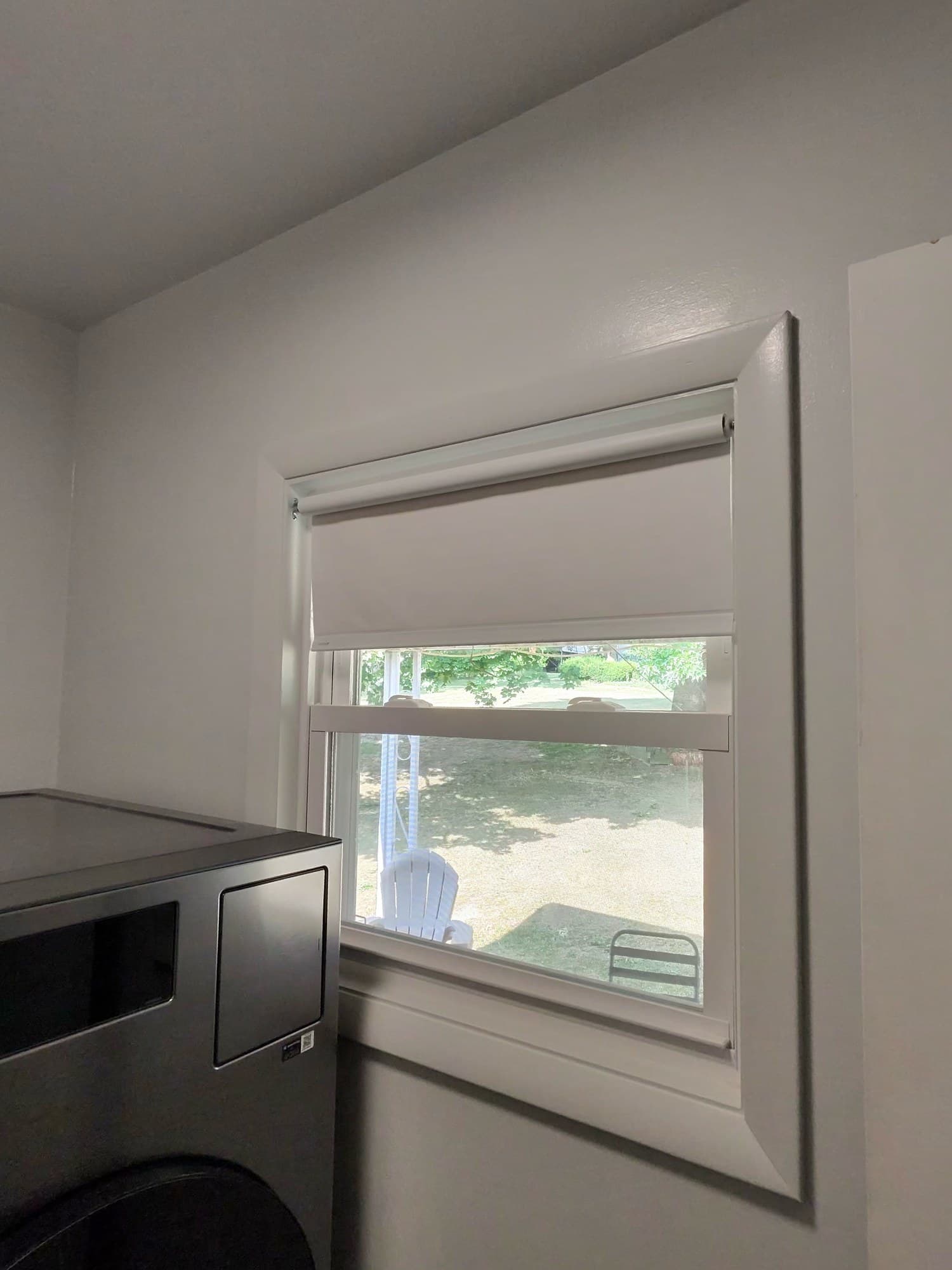 Finished white window trim and roller shade beside the laundry appliance.