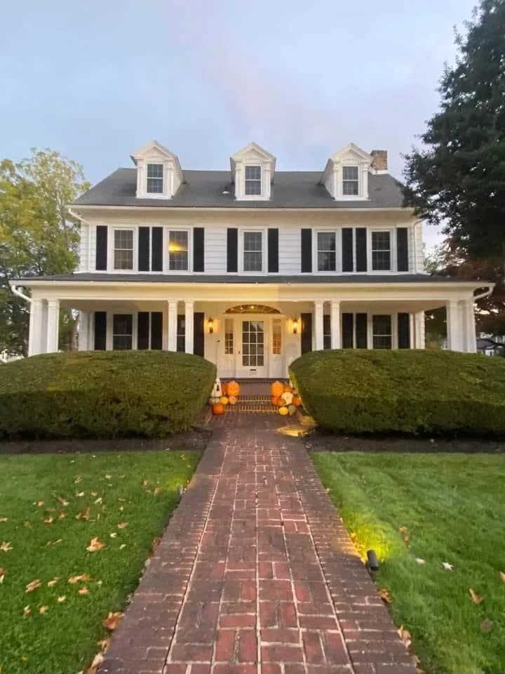 Wide front view of a house with dormer windows, a porch, and contrasting shutters.