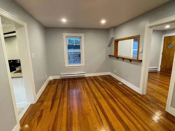 Interior room with warm-toned floorboards, light walls, recessed lights, and a trimmed wall opening.