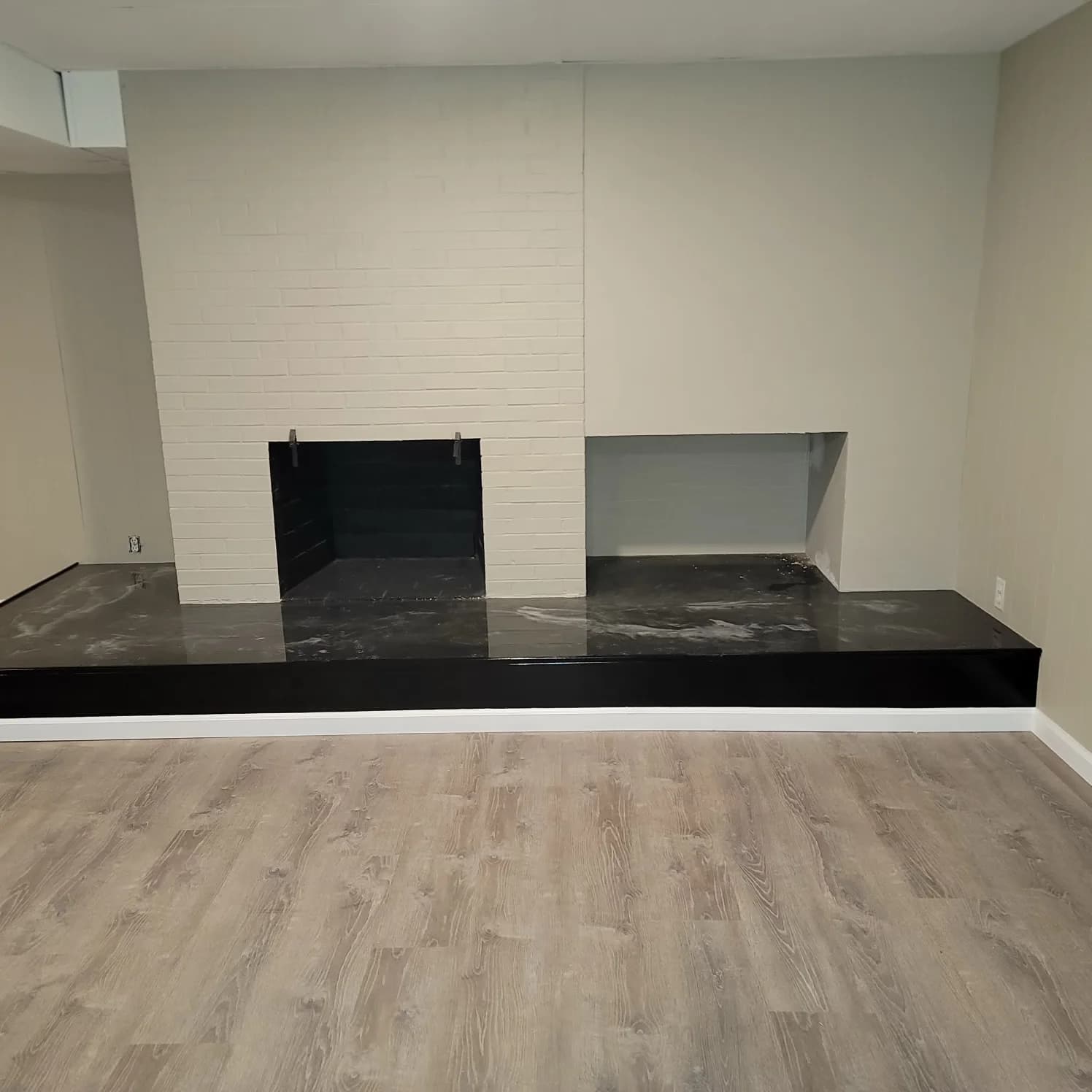 Light fireplace surround above a dark hearth beside a rectangular side opening.