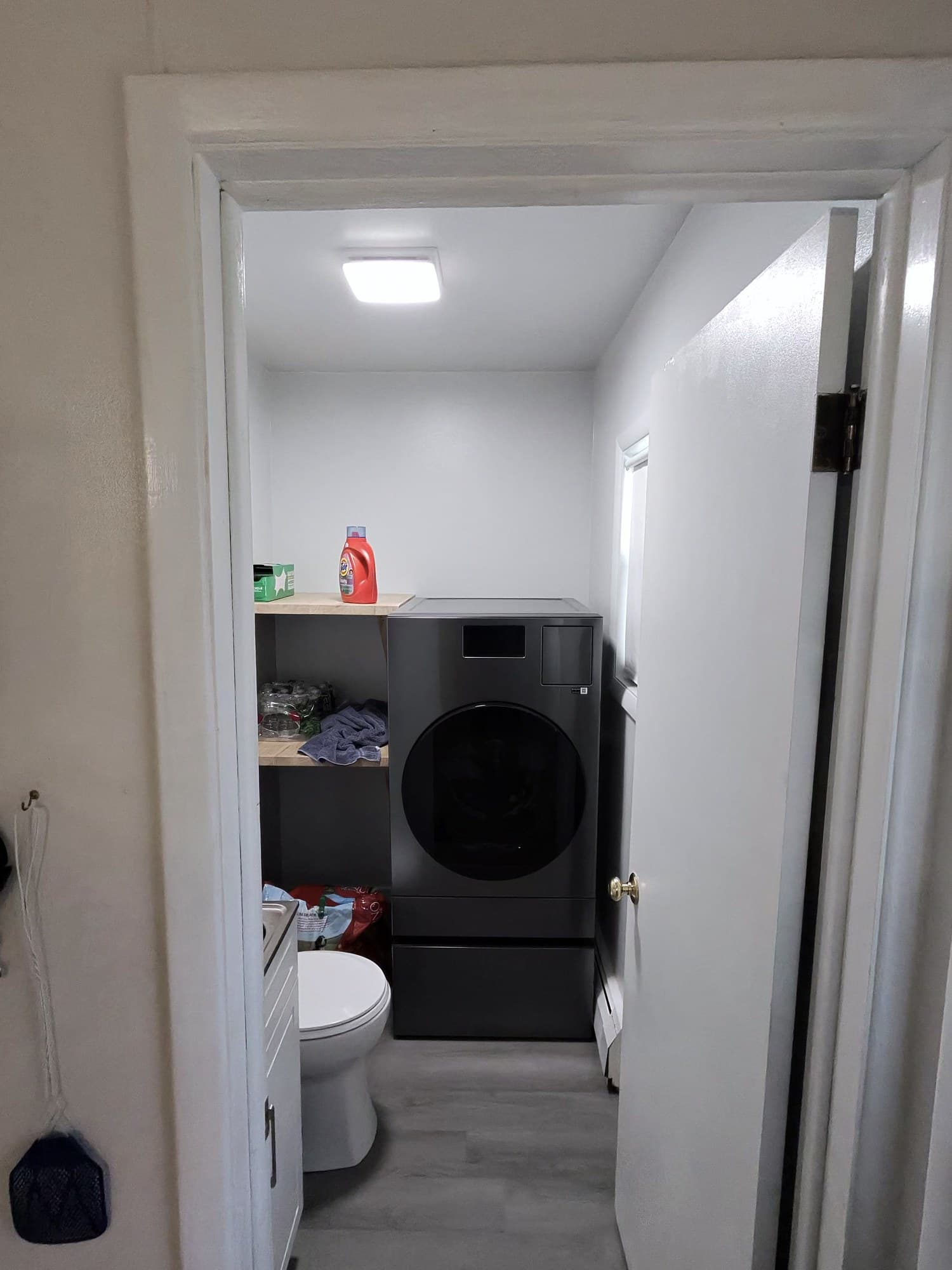 Doorway view of the finished Hamburg laundry and half-bath with gray flooring and charcoal washer.