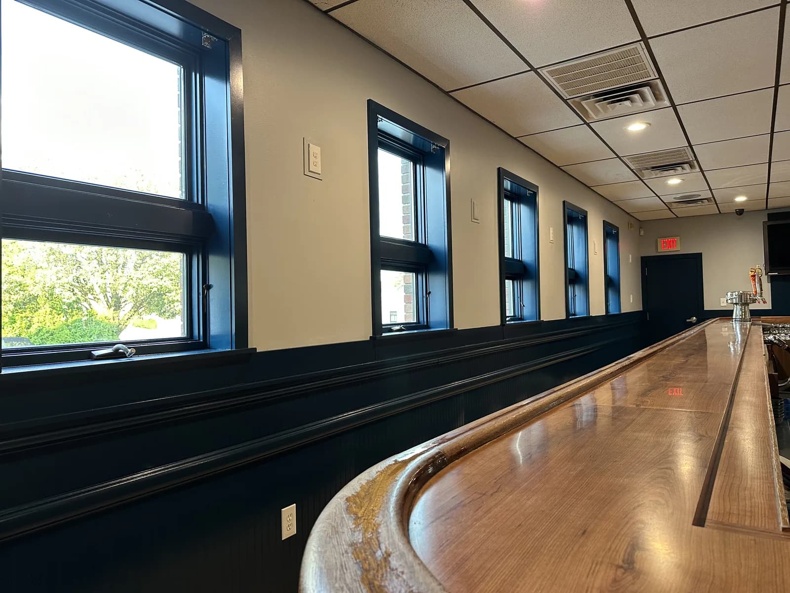 Row of windows with dark trim beside a long commercial bar seating area.