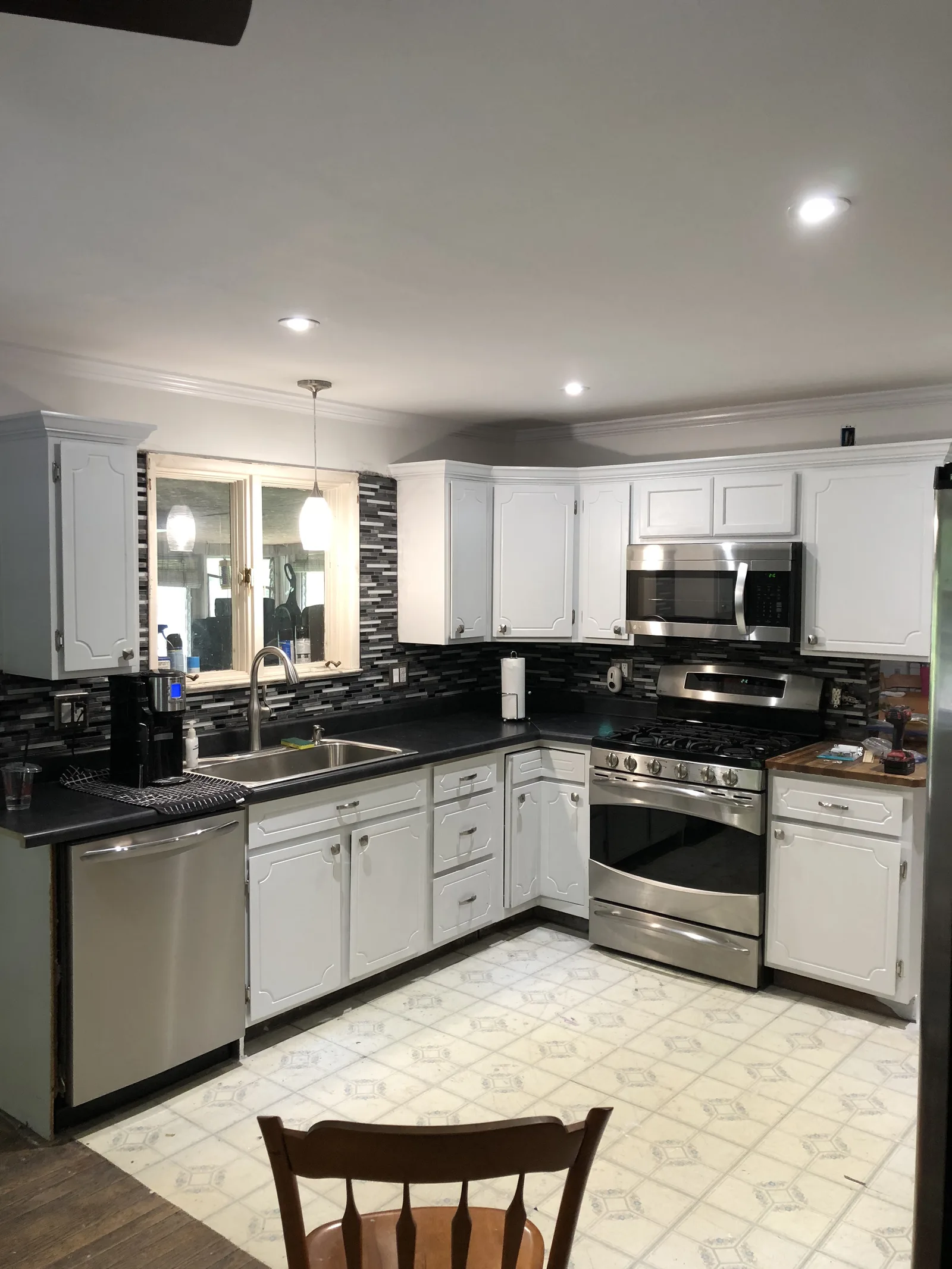Kitchen corner with white cabinets, dark countertops, stainless appliances, and recessed lights.